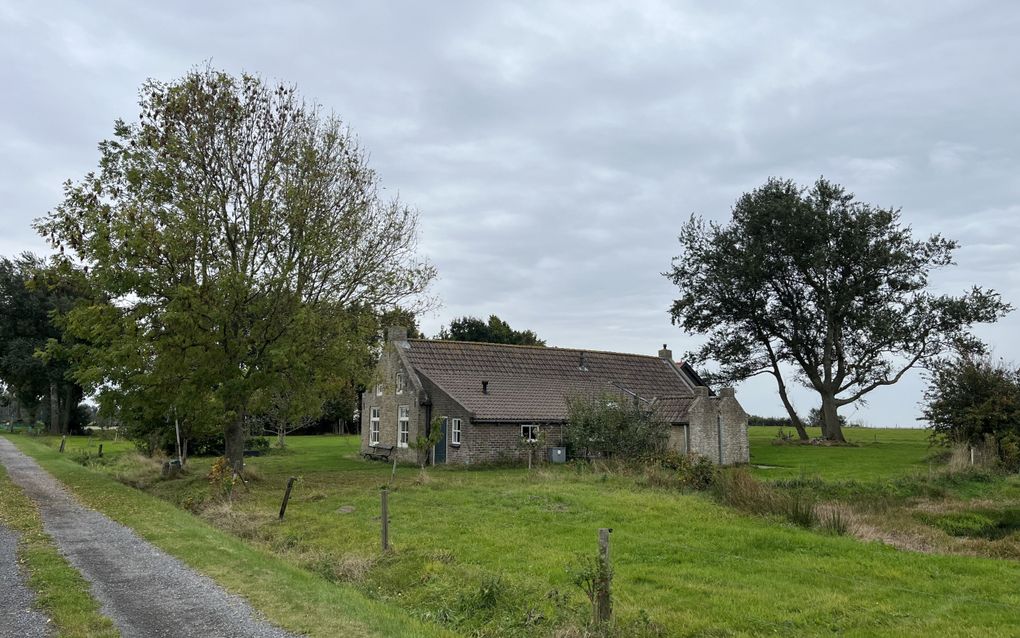 Een oud huisje staat midden in het land. Eromheen staan bomen. Links een karrenspoor voor het huisje langs.