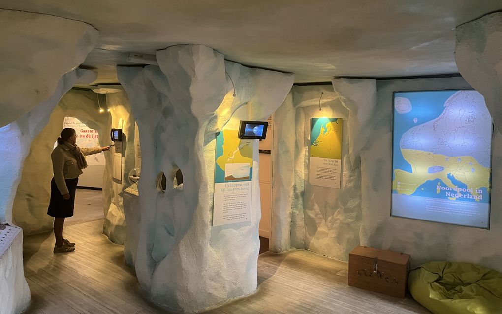 Een vrouw bekijkt een scherm in een expositieruimte. De aankleding van de ruimte is wit en grillig, het lijkt een ijshol. Aan de wanden hangen schermen en kaarten.