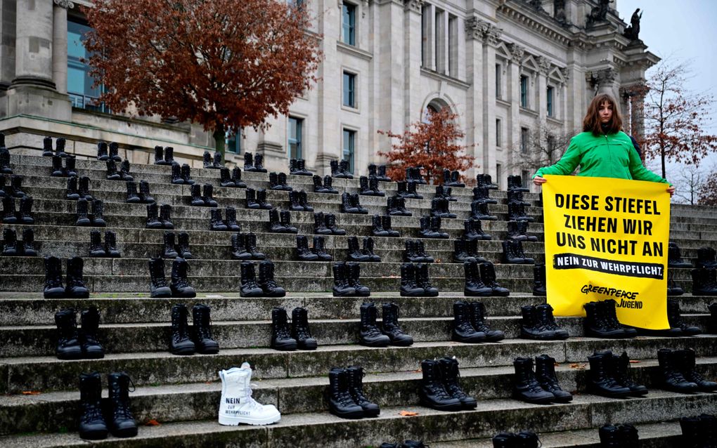 Tientallen paren zwarte soldatenlaarzen staan op traptreden, terwijl iemand een gele protestvlag vasthoudt.