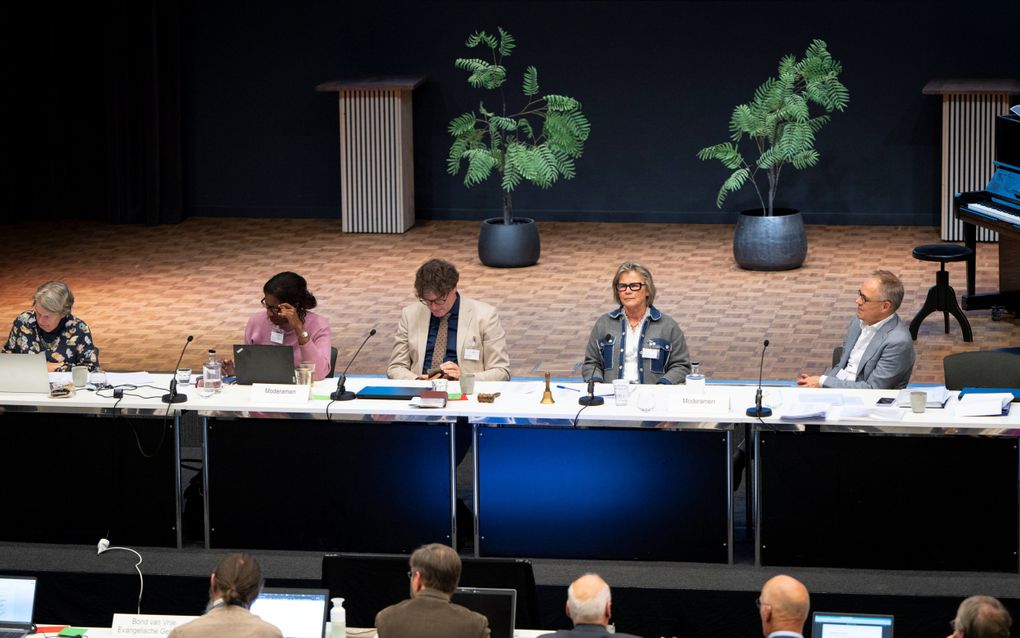 Drie vrouwen en twee mannen achter een langwerpige tafel met microfoons.