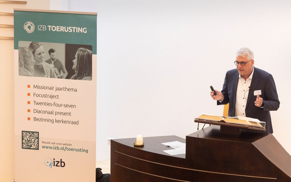 Man met grijs haar en een bril achter een katheder.