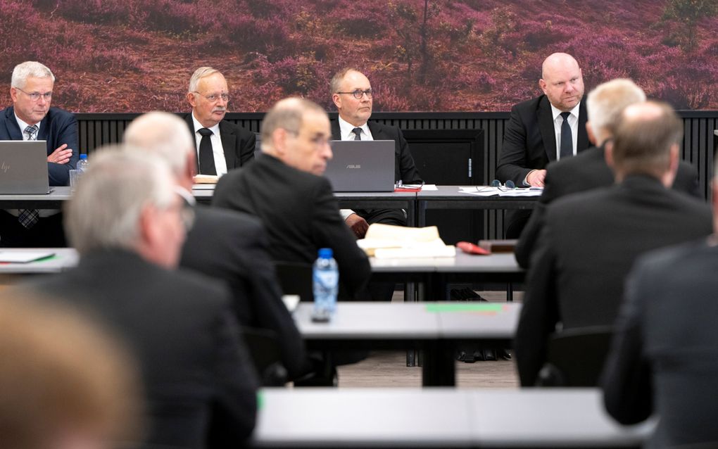 Mannen in pak zitten achter tafels in een vergaderzaal.