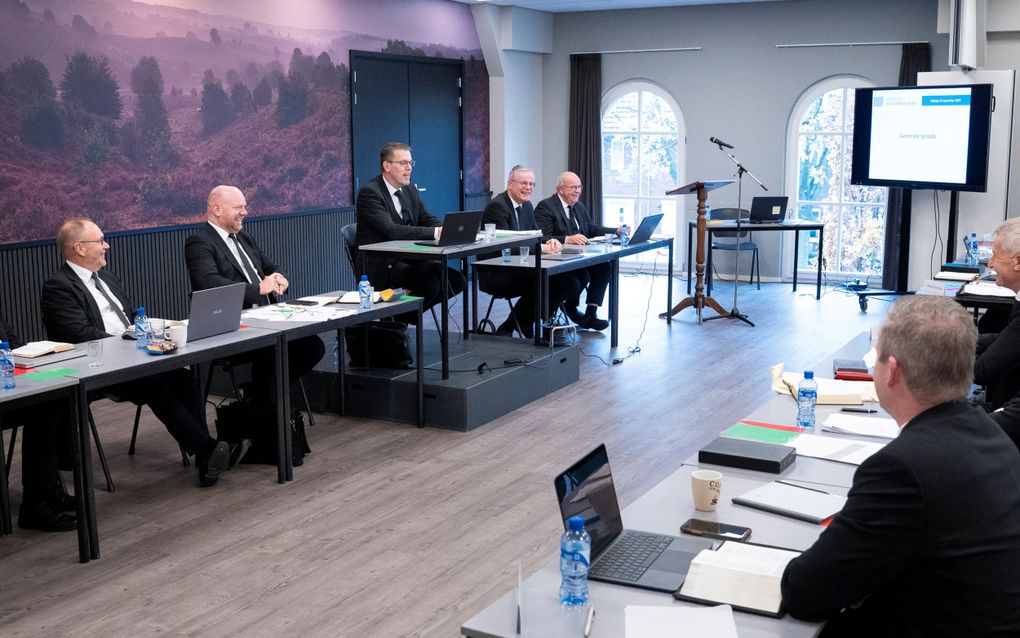 Mannen in pak zitten achter tafels in een vergaderzaal.