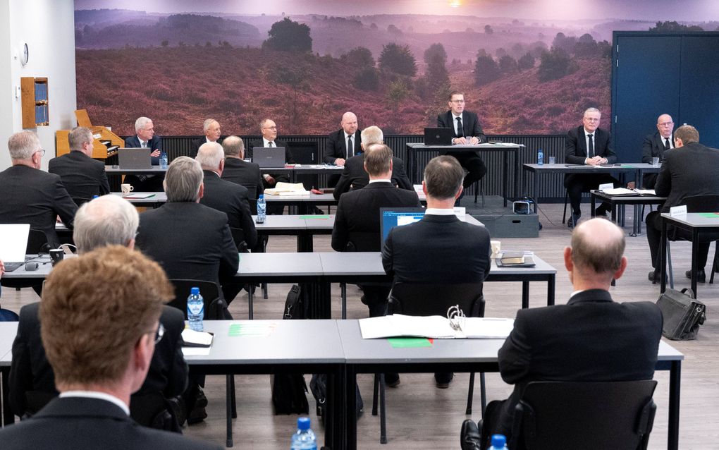 Mannen in pak zitten achter tafels in een vergaderzaal.