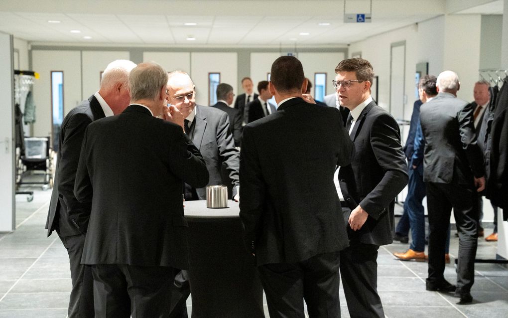 Mannen in pak staan rond een tafel in de hal van een kerk.