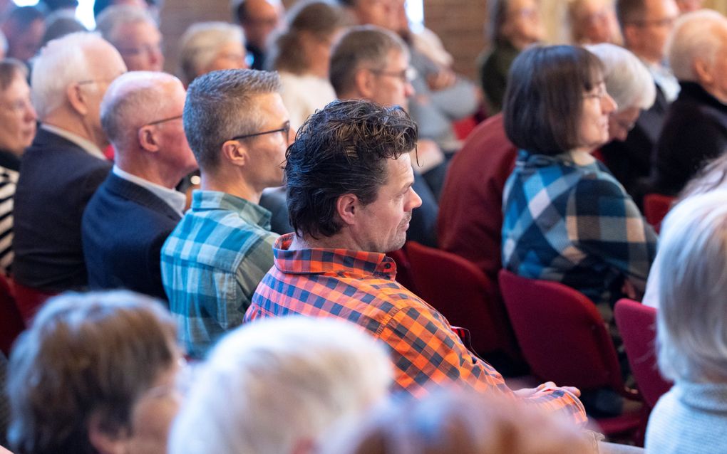 Mensen op rijen stoelen, schuin van opzij gezien.