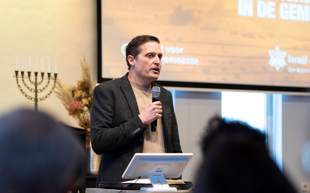 Een man met een colbert aan en met een microfoon in zijn hand.