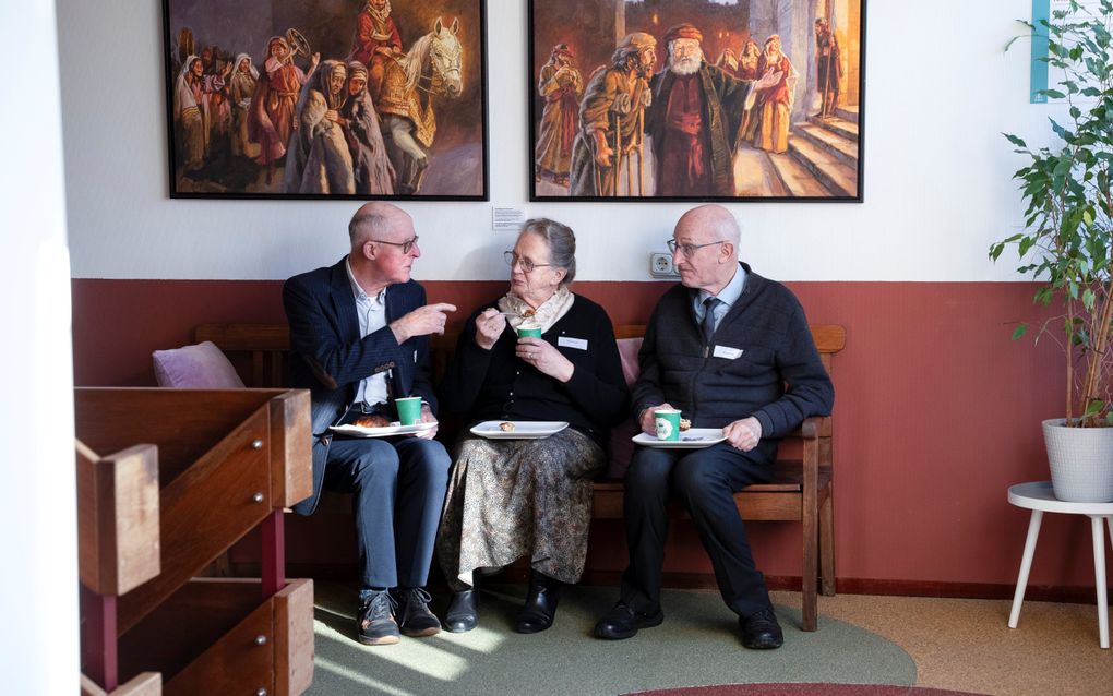 Twee mannen en een vrouw zitten op een bank met een blad met eten voor zich.