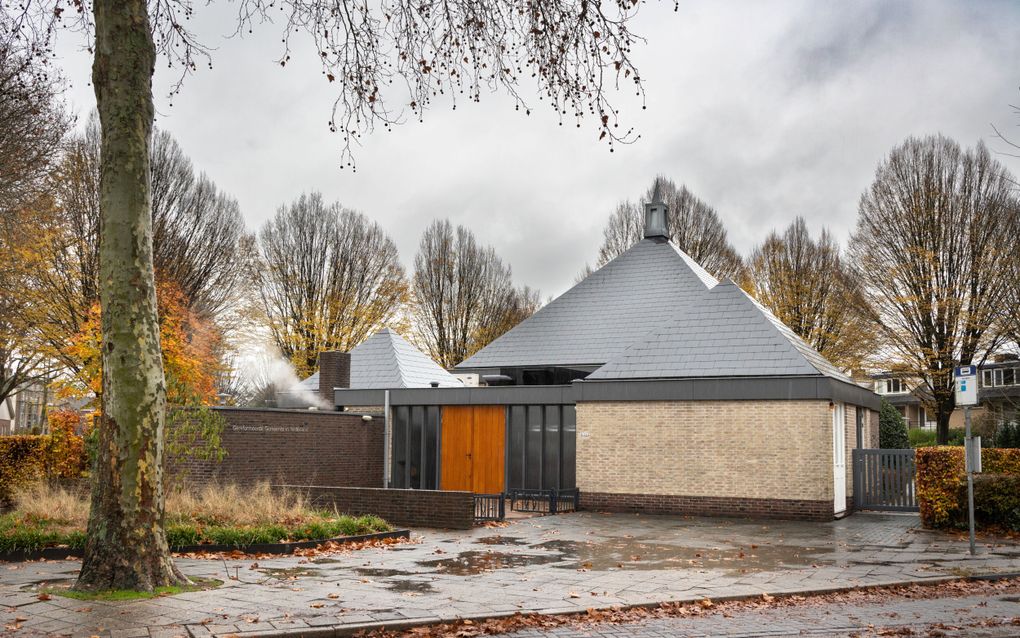 Een geel-grijs kerkgebouw met drie piramidevormige leien daken. De achterste piramide is het grootst.