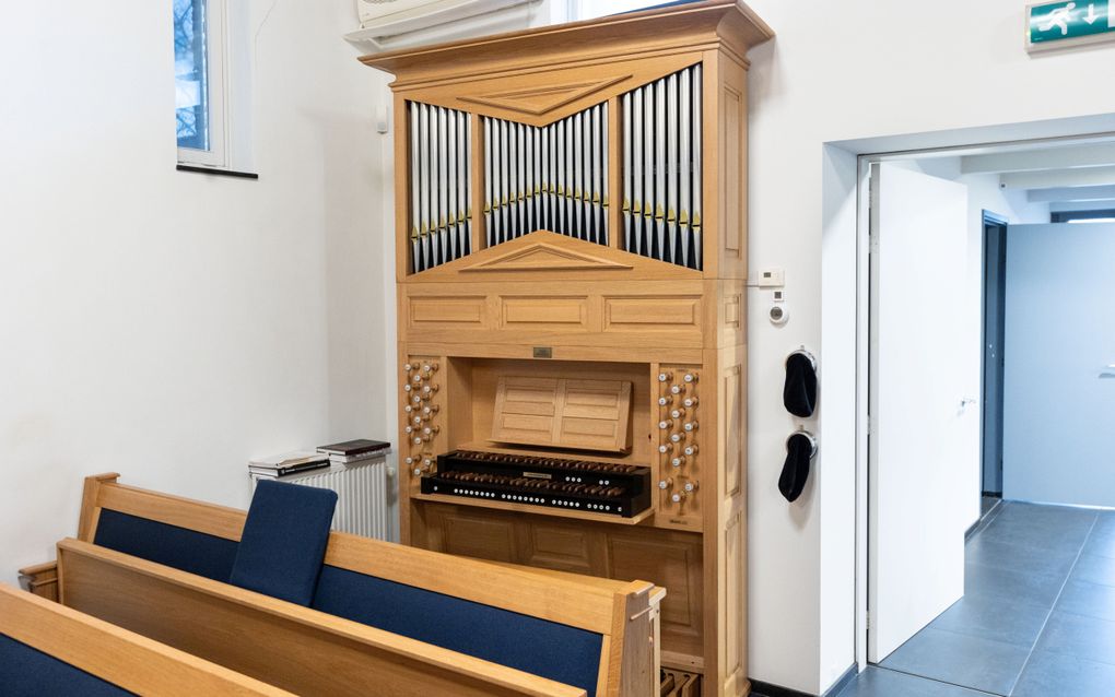 Een geelbruin gelakt kerkorgel staat tegen een witte wand.