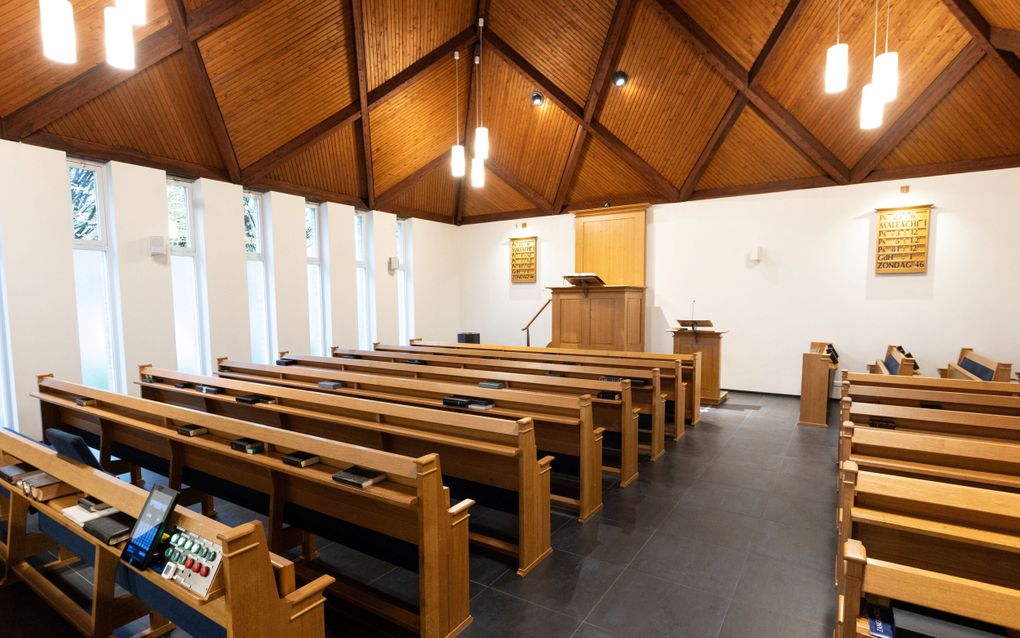 Een kerkzaal met kerkbanken, plafond van schrootjes en op de achtergrond een kansel en katheder.