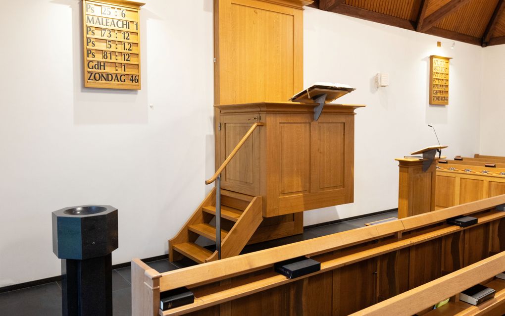 Een geelbruin gelakte kansel. Links ervan een zwart doopvont. 