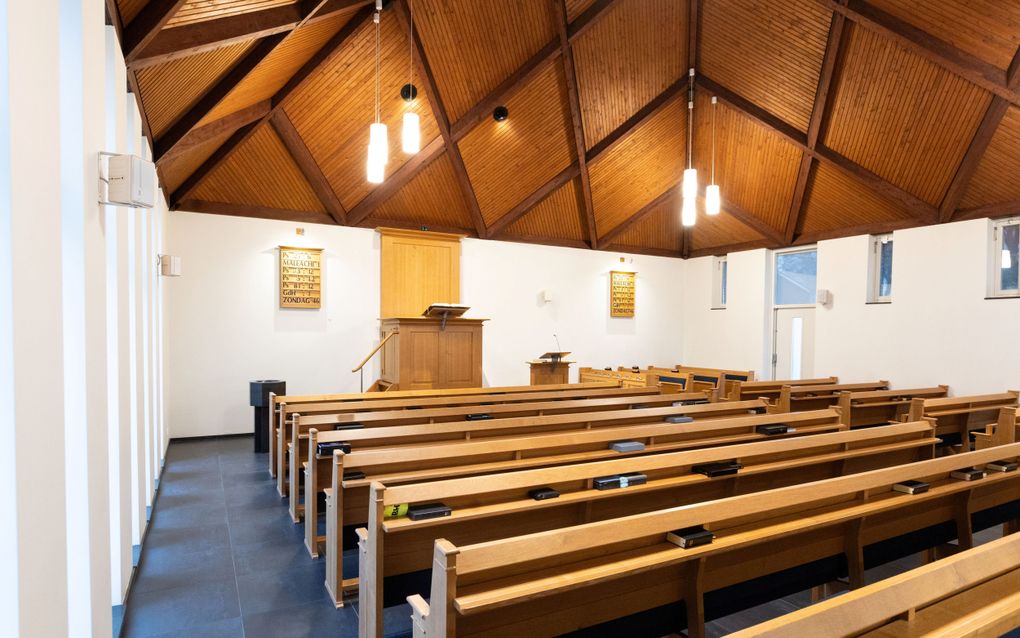 Een kerkzaal met kerkbanken, plafond van schrootjes en op de achtergrond een kansel, doopvont en katheder.