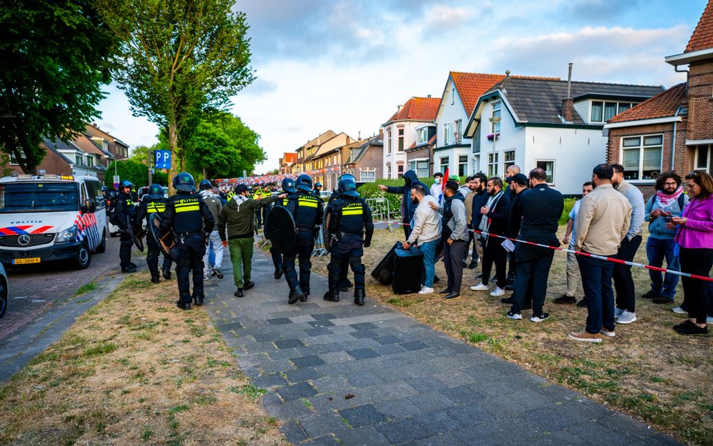 Mensen achter een lint. Daarnaast met schilden bewapende politiemensen.