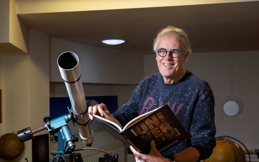 Man bladerend in een boek naast een telescoop.