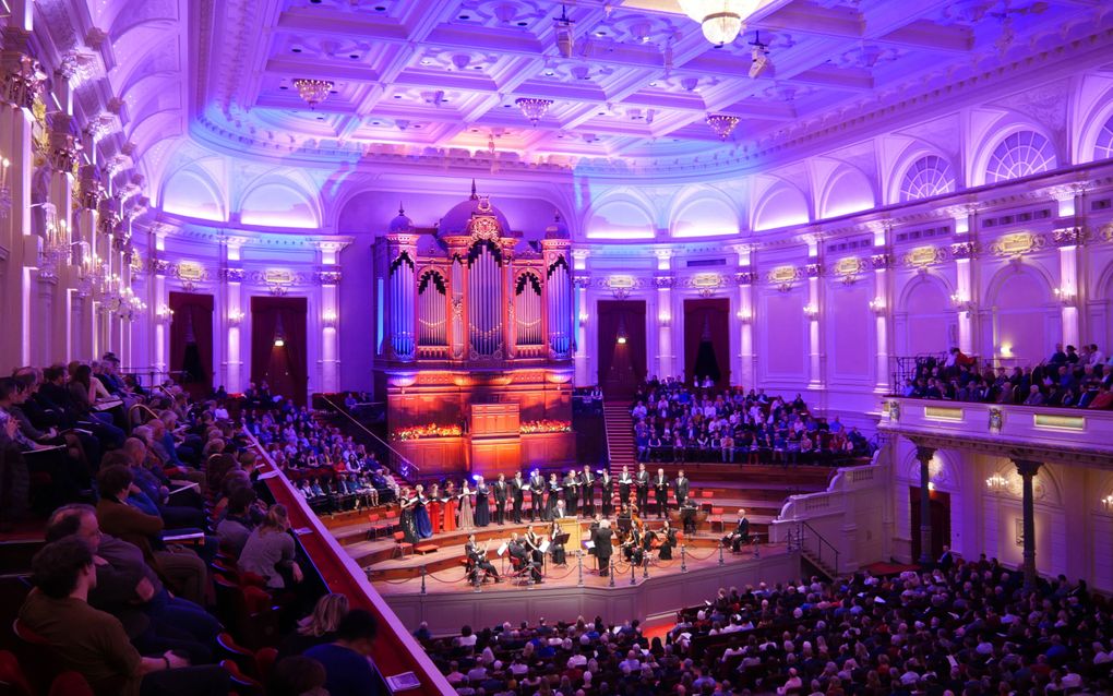 Blauw verlicht Concertgebouw met op het podium een koor en orkest met dirigent. Daarachter een enorm orgel en rijen vol luisteraars om het podium heen.