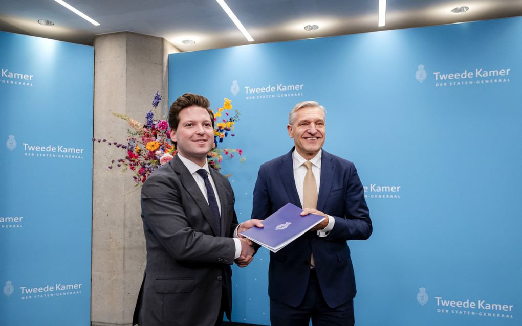 Twee mannen in pak schudden elkaar de hand, waarbij een rapport wordt overhandigd.