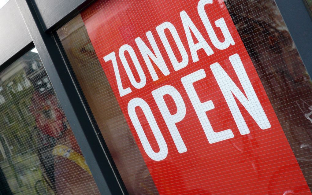 Een rode poster met in witte letters ‘zondag open’ achter een winkelraam.