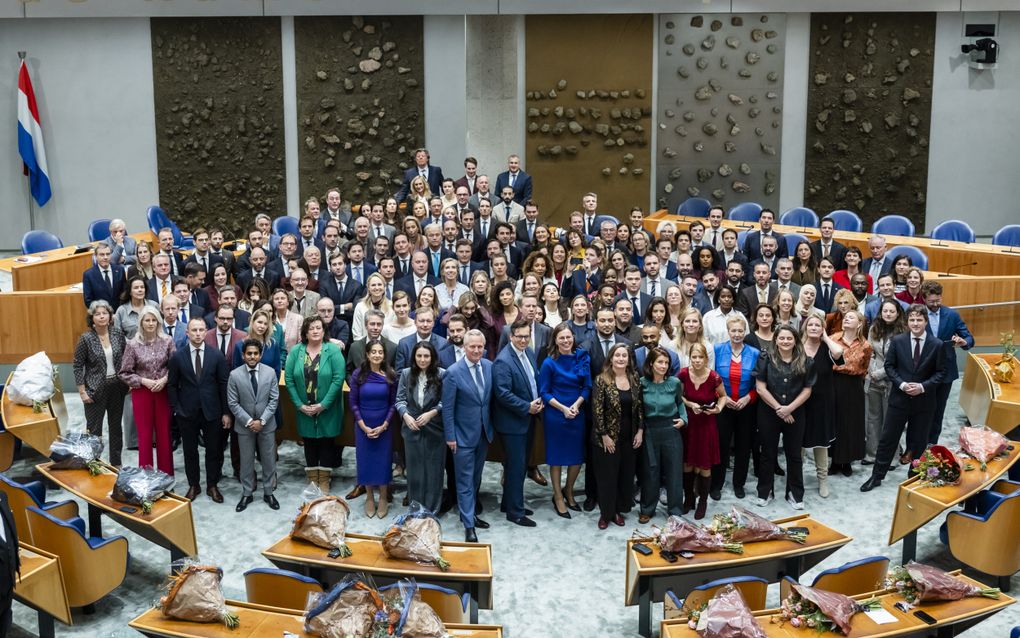 Een groep mensen in  de Tweede Kamer, op de voorgrond boeketten voor de nieuwe kamerleden.
