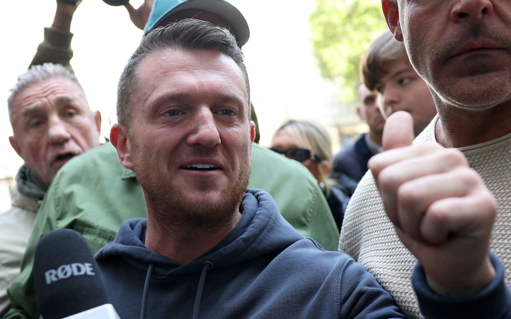 Een man met baardje, trui met capuchon, steekt zijn duim op. Hij wordt omringd door een groep mensen.