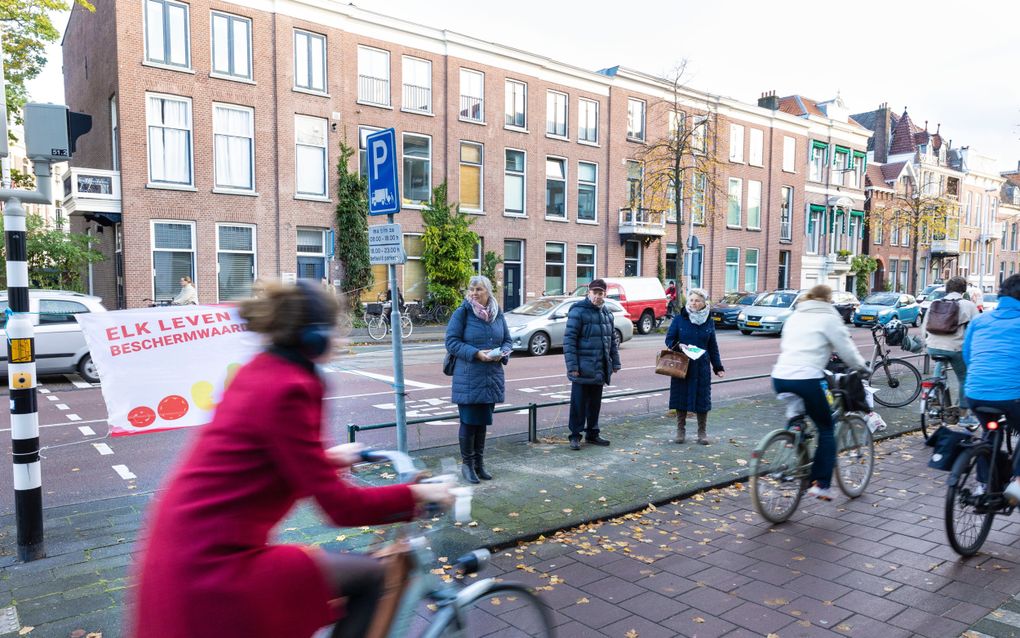 Mensen staan op de stoep met flyers, terwijl fietsers voorbij fietsen 