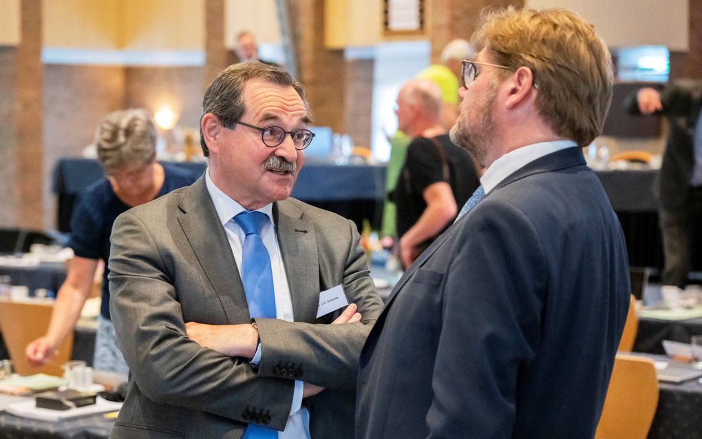 Twee mannen staan in een vergaderzaal met elkaar te praten.