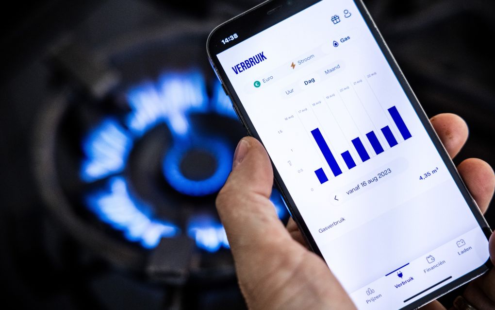 Een overzicht op het scherm van een martphone van het energieverbruik van een huishouden, met op de achtergrond een brandend gasfornuis.