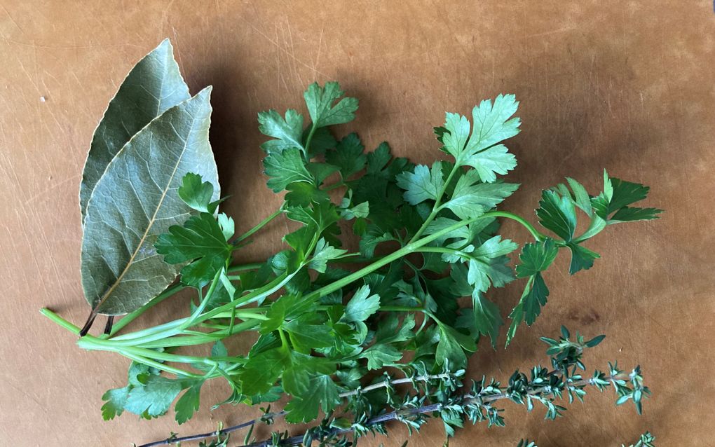 Takjes groene kruiden en laurierblaadjes op een lichtbruine ondergrond.