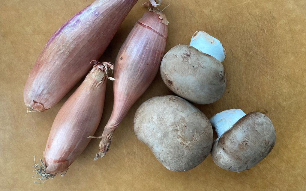 Op een lichtbruin werkblad liggen drie sjalotjes en drie champignons.