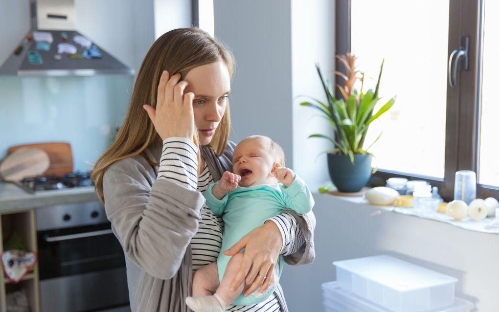 Vrouw met huilende baby in haar armen. Ze grijpt naar haar hoofd.