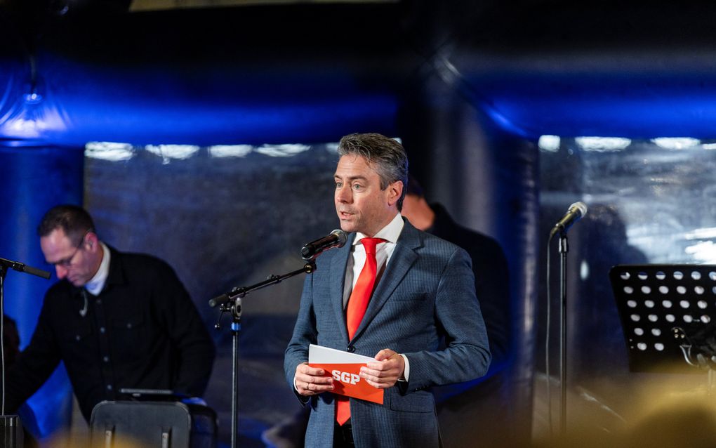 Man in pak met oranje stropdas op podium. Hij heeft een kaart vast met SGP erop.