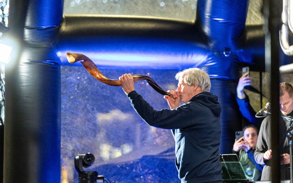 Man in blauw vest blaast op een grote ramshoorn.
