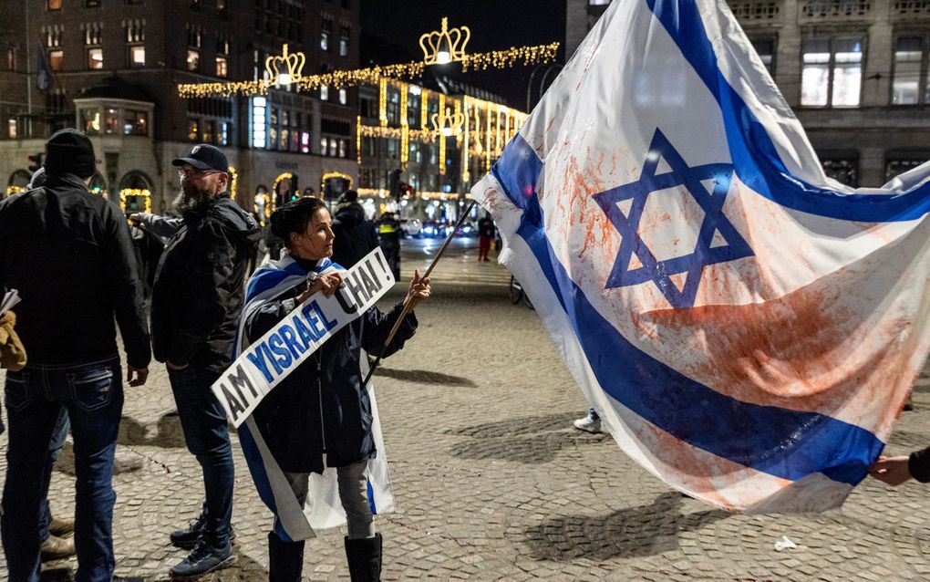 Vrouw met een grote Israëlvlag die besmeurd is met rode verf.