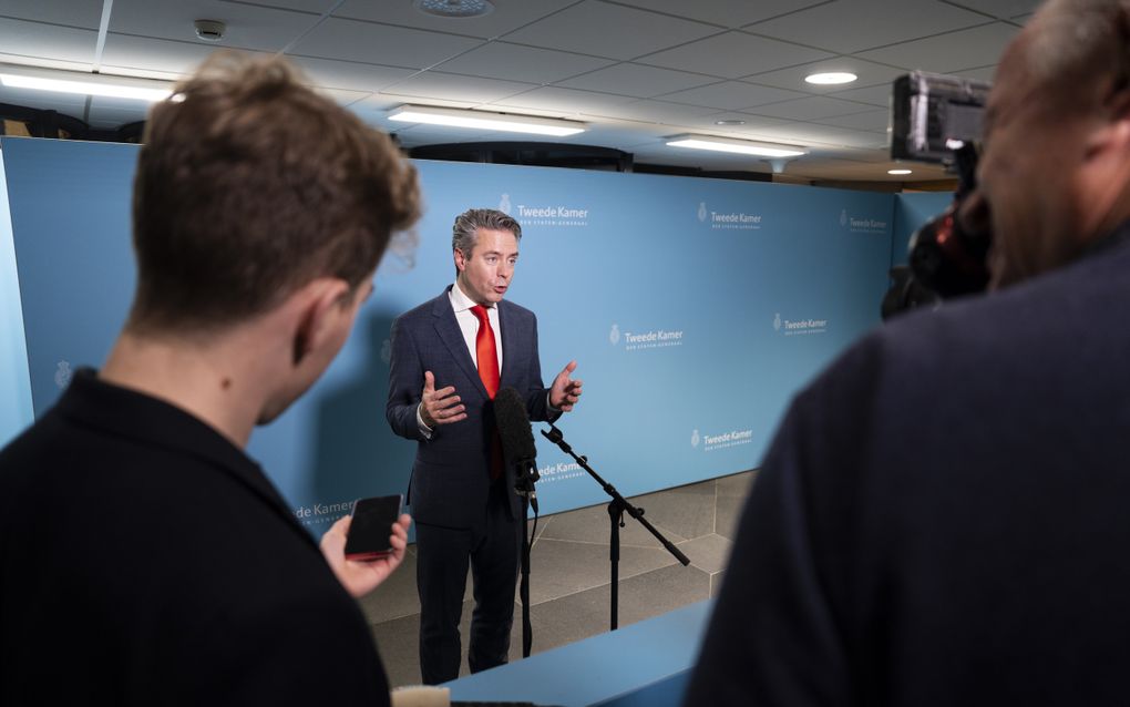 Man in pak staat tegenover journalisten van wie er een aantal op de rug is gefotografeerd.