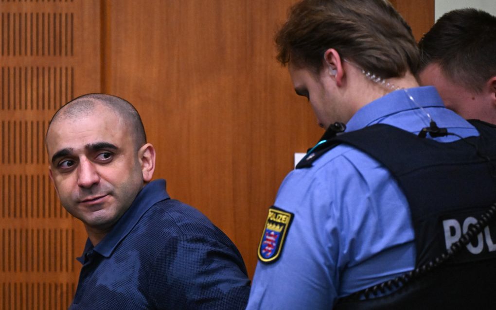 Een man wordt een rechtszaal binnengeleid door politieagenten. 