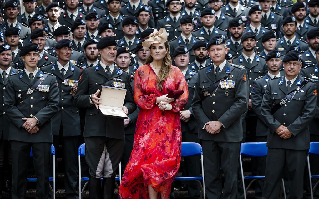 Vrouw in rode jurk tussen militairen in uniform.