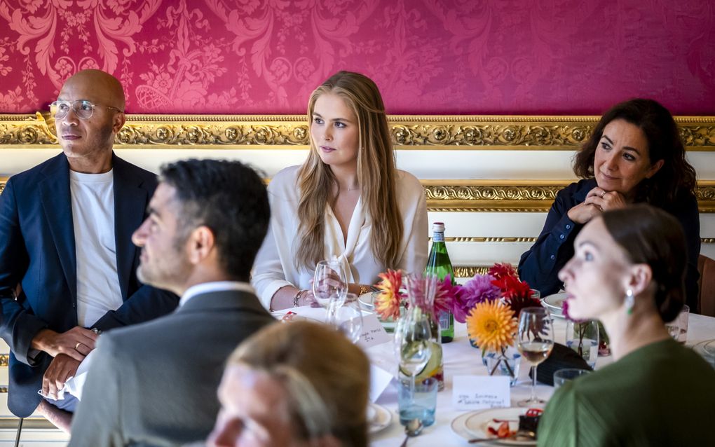Jonge vrouw zit aan tafel naast een man en een vrouw.
