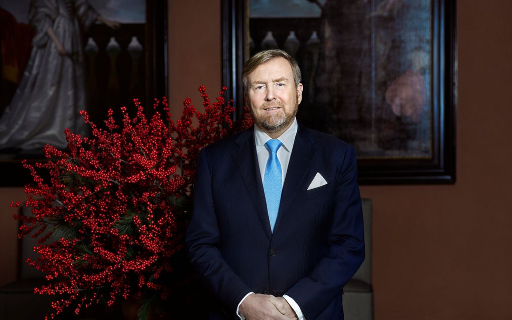 Man in pak met stropdas voor takken met rode bessen en twee schilderijen