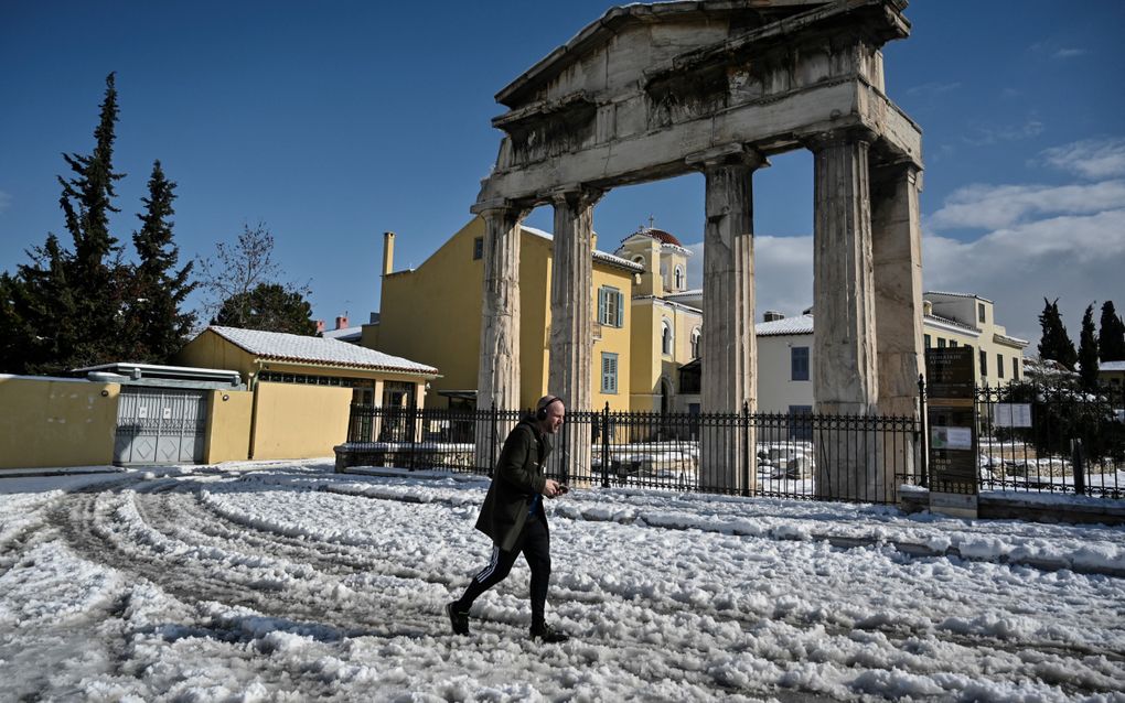 Een man loopt door de sneeuw voor de restanten van een oud Grieks bouwwerk met pilaren.