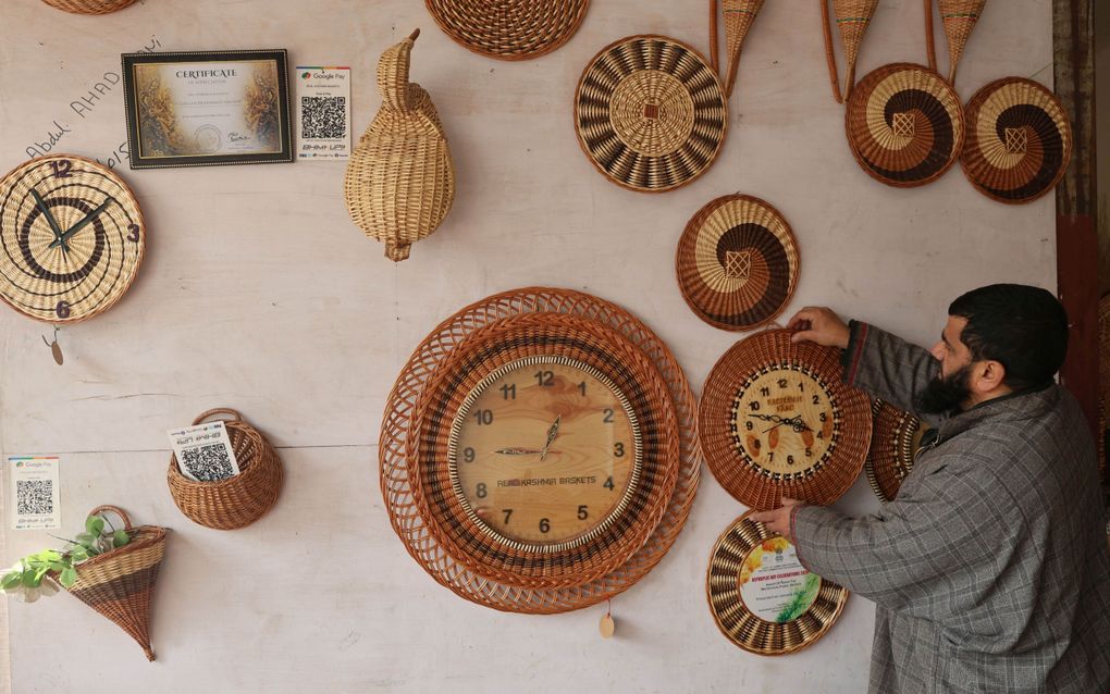 Een man met baard hangt een klok aan de muur.