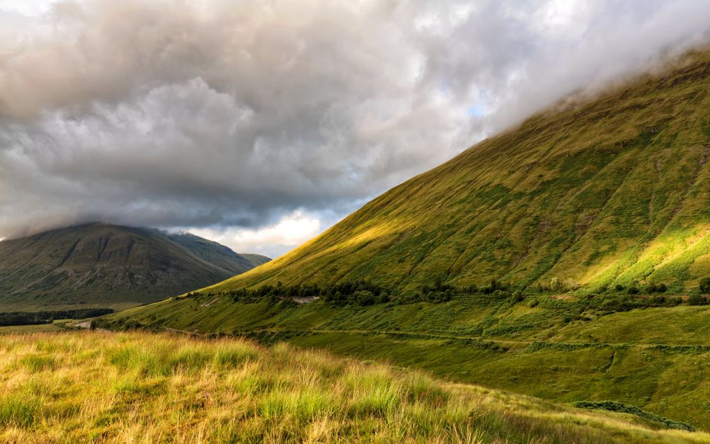 Langs een steile groene berghelling loopt een pad.
