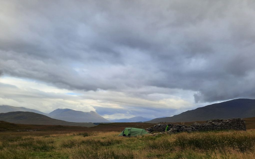 Een groene tent staat in een grasveld naast een stenen muurtje.