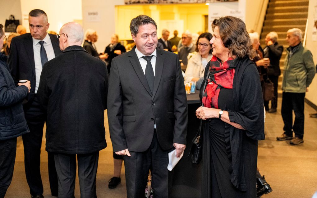 Man in zwart pak praat met vrouw met zwarte jurk en rode sjaal.