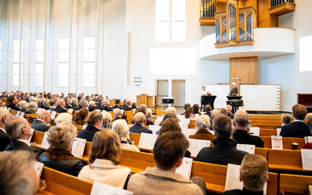Luisterende mensen van chetren gezien, in een kerkgebouw. Man met wit haar interviewt meisje, vooraan op podium.