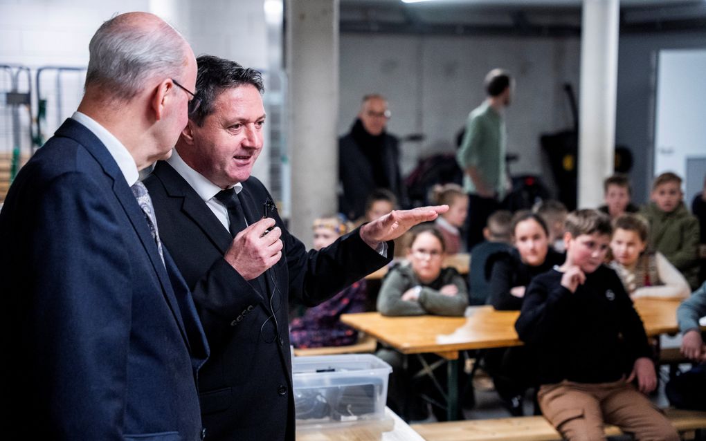 Man in zwart pak praat in microfoon.