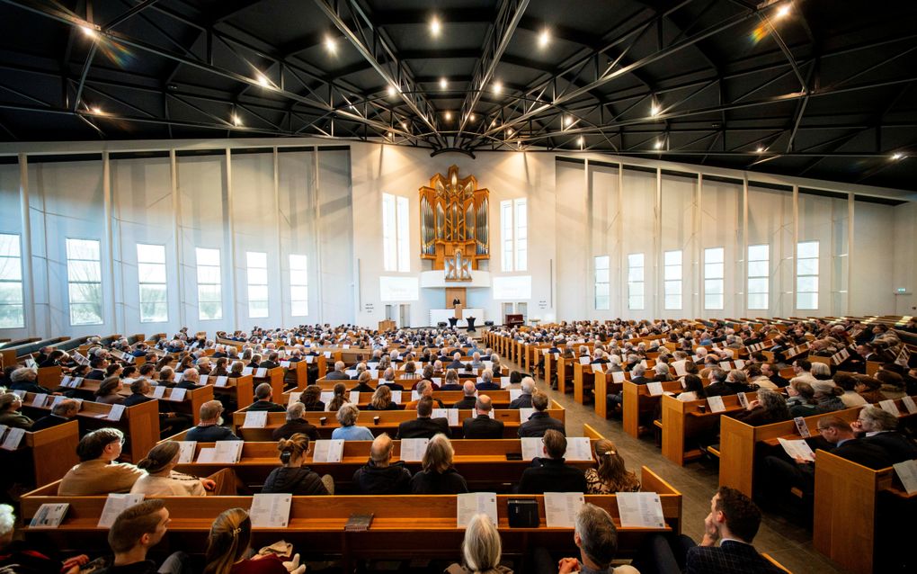 Volle kerkbanken, van achteren gezien.