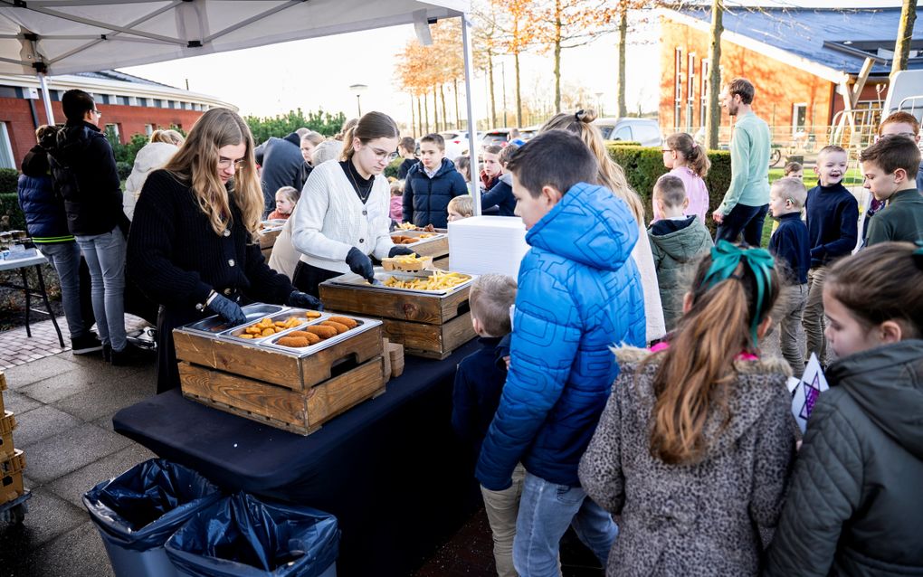 Meisjes scheppen buiten onder afdak patat en kroketten op.