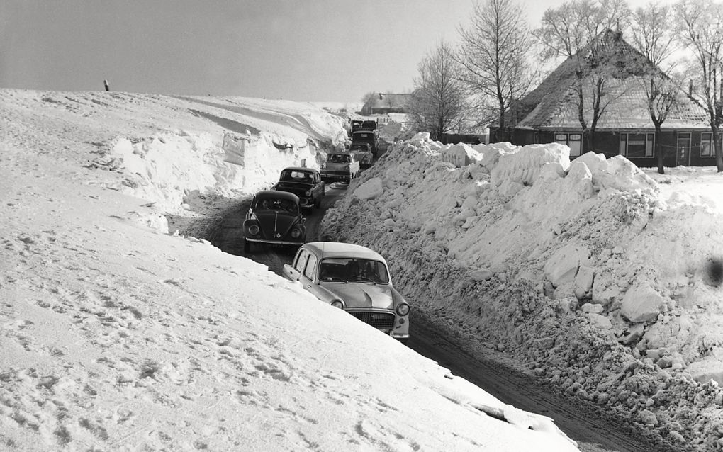 Zwart-witfoto waarbij auto’s in een rijtje door twee muren van sneeuw heen rijden.