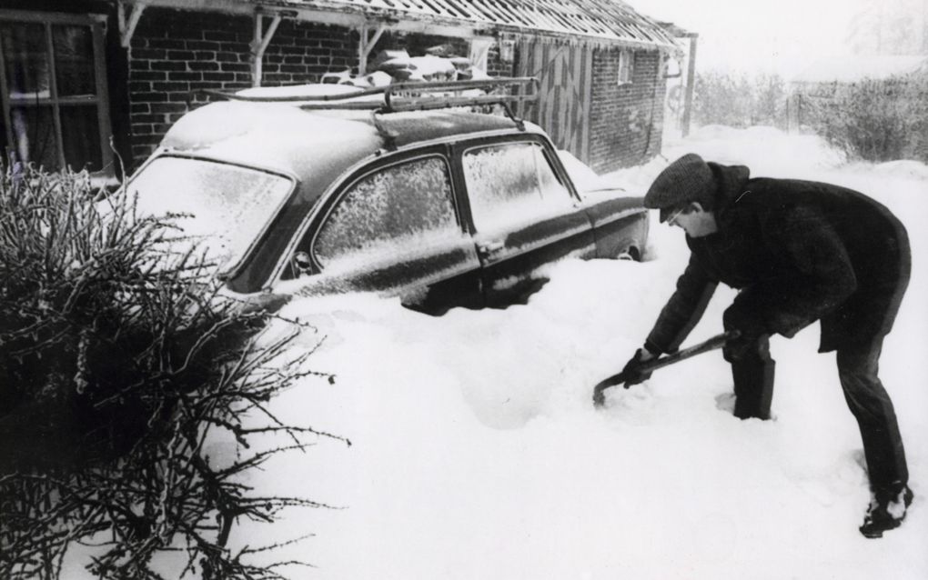 Zwart-witfoto waarbij man zijn auto uit de sneeuw graaft. 