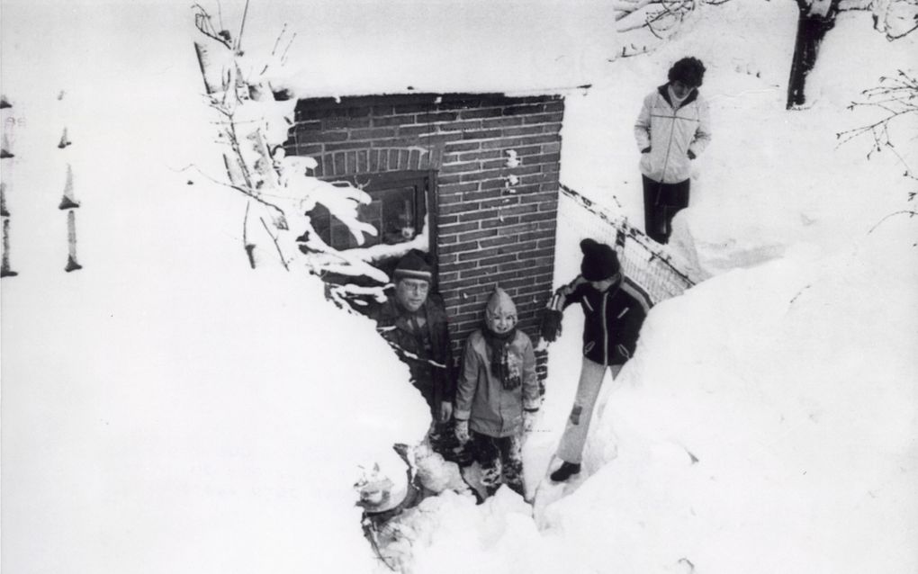 Zwart-witfoto waarbij gezin voor de voordeur van hun huis staat met muren van sneeuw eromheen. 